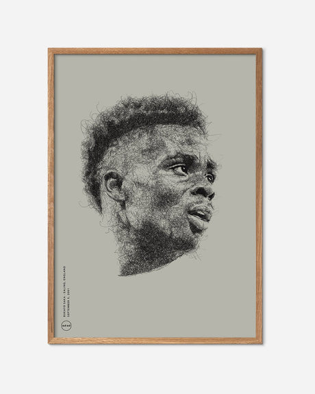 Beige fodboldplakat med kunstnerisk sort stregtegning af Bukayo Saka i egetræsramme